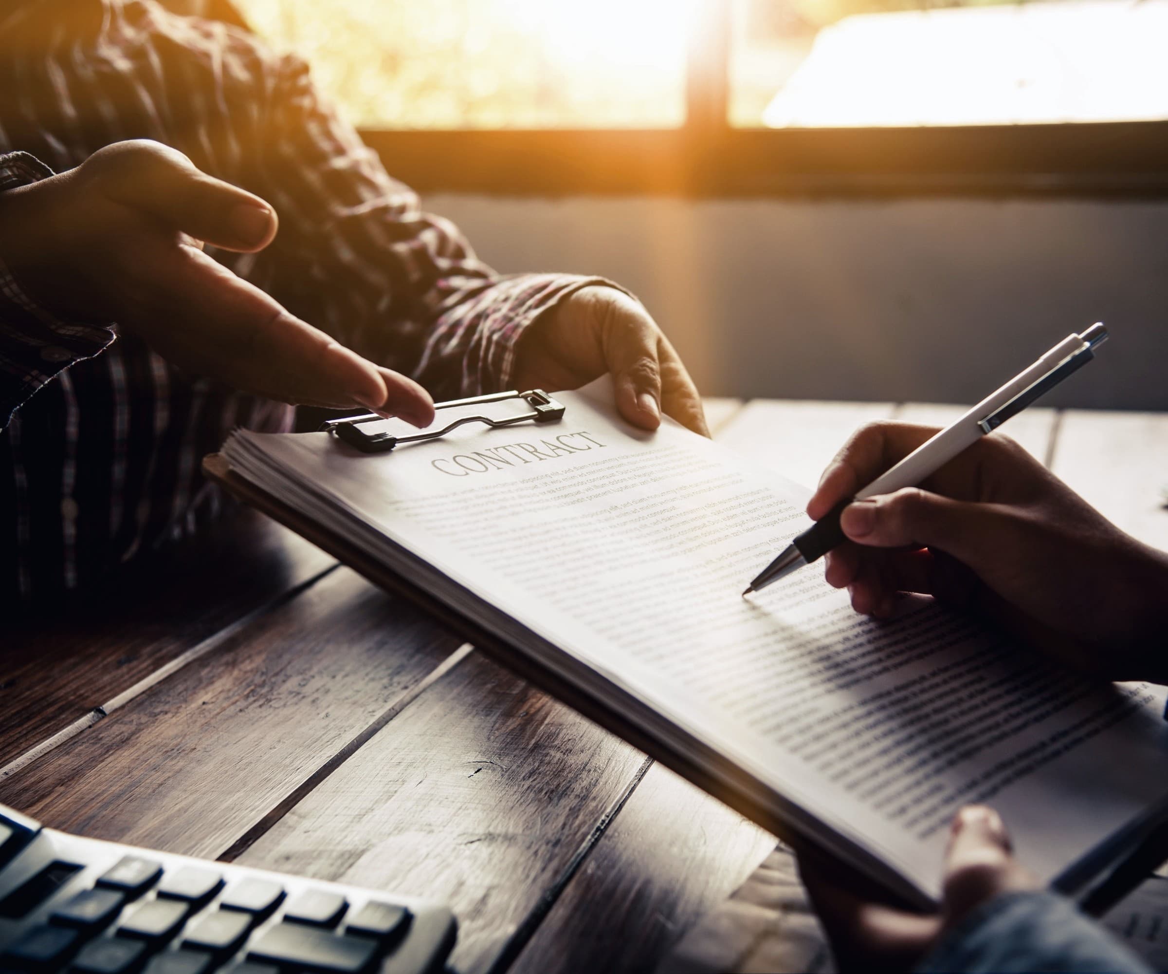 Two people signing a printed contract at a desk.