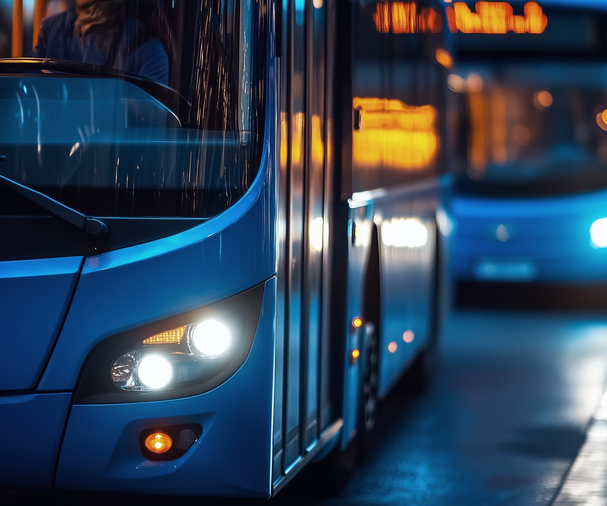 City transit buses lined up along a street in the evening.